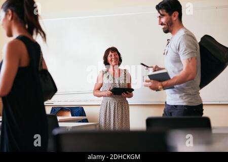 Ältere Frau lächelt, während sie das digitale Tablet im Klassenzimmer hält Stockfoto