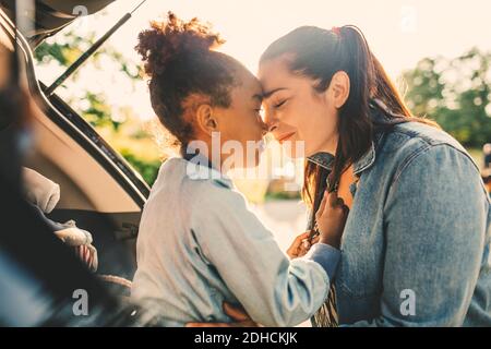 Lächelnde Frau und Tochter, die mit den Augen von Angesicht zu Angesicht sitzen Während des Picknicks im Kofferraum geschlossen Stockfoto