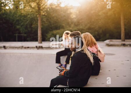 Nachdenkliche Teenager-Mädchen halten Handy, während mit Freunden sitzen Im Skateboard Park Stockfoto