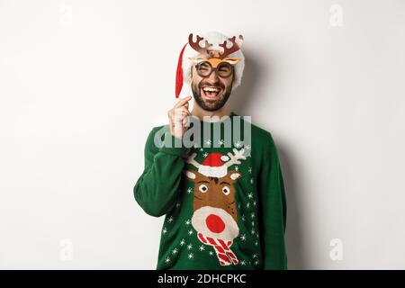 Weihnachten und Feiertage Konzept. Lächelnder bärtiger Mann in Weihnachtsmann Hut glücklich, hält Party-Maske für Neujahr, feiert Weihnachten Stockfoto
