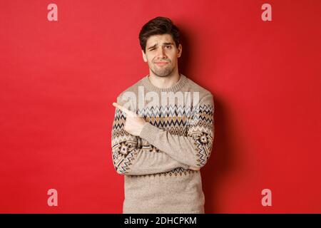 Bild von skeptischen und unzufrieden Mann in weihnachten Pullover, zeigt auf die obere linke Ecke unamüsiert, zeigt schlechte Weihnachtsgeschenk, stehen Stockfoto