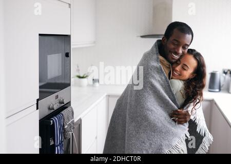 Liebevolle junge gemischte Ethnizität Paar kuscheln, während in der Küche stehen Zusammen in kuschelige Decke gewickelt Stockfoto
