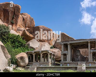 Hampi, Karnataka, Indien - 4. November 2013: Nandi Monolith Statuentempel in Kombination mit riesigen braunen Felsbrocken, die oben auf einem Hügel unter blauem Himmel sitzen. Stockfoto