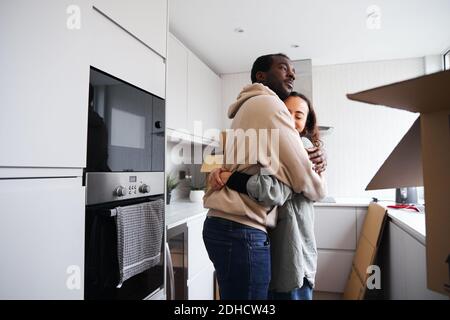 Junge gemischte Ethnizität Paar in der Küche des neuen Hauses stehen Beim Auspacken der Entnahmeboxen umarmt Stockfoto
