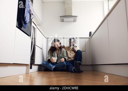 Junge gemischte Ethnizität Paar feiern bewegenden Tag in Küche sitzen Auf dem Boden trinken heiße Getränke zusammen Stockfoto