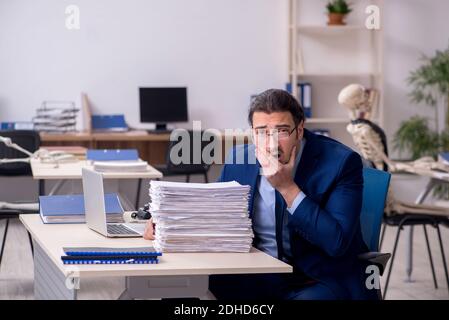 Junger männlicher Angestellter mit Skeletten im Büro Stockfoto