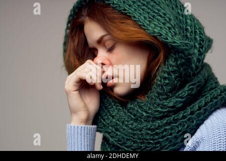 Frauen in einem gestrickten Kopfschmuck und in einem blauen Pullover Auf grauem Hintergrund gesundheitliche Probleme laufende Nase Stockfoto