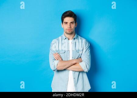 Bild von schönen kaukasischen Mann in Casual Outfit, suchen ernst und zuversichtlich, vor blauem Hintergrund stehen Stockfoto