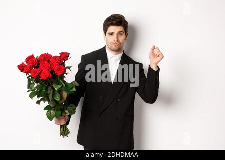 Bild von eleganten und frechen Mann in schwarzem Anzug, zuversichtlich und hält Strauß von roten Rosen, gehen auf ein romantisches Date, Stan Stockfoto