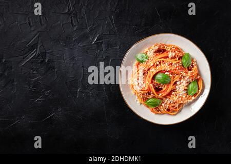 Spaghetti mit Tomatensauce, geriebenem Parmesan-Käse und Basilikum, Overhead-Aufnahme auf schwarzem Hintergrund Stockfoto