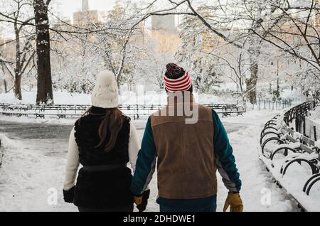 Ein flacher Fokus eines Paares, das Hände hält und geht Rund um einen Park im Winter im Schnee bedeckt Stockfoto
