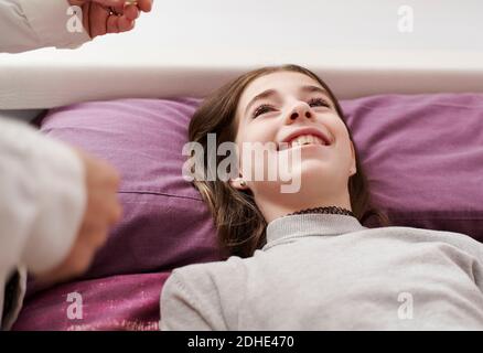 Detail eines Mädchens in ihrem Bett lächelnd auf den Arzt, der sie zu Hause besucht. Hausarzt Konzept Stockfoto
