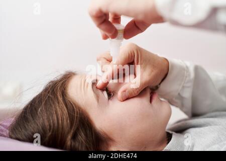 Detail einer Ärztin, die lächelt und einem kleinen Mädchen in ihrem Bett Augentropfen gibt. Hausarzt Konzept Stockfoto
