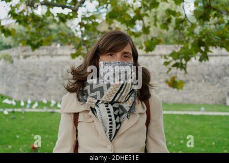 Portait einer Frau mit weißem Mantel und medizinischer Maske, die ein grünes Feld von einem Park aus beobachtet. Urlaubskonzept Stockfoto