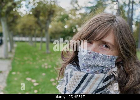 Portait einer Frau mit weißem Mantel und medizinischer Maske, die ein grünes Feld von einem Park aus beobachtet. Urlaubskonzept Stockfoto