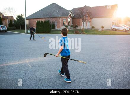 Zwei Jungen spielen im Herbst auf einer Wohnstraße Straßenhockey. Stockfoto