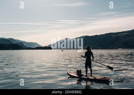 Eine junge Frau paddelt an einem sonnigen Tag auf dem Columbia River mit einem SUP. Stockfoto