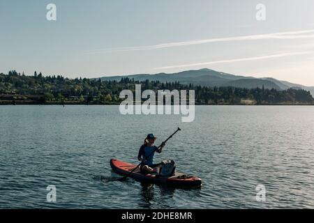 Eine junge Frau paddelt an einem sonnigen Tag auf dem Columbia River mit einem SUP. Stockfoto