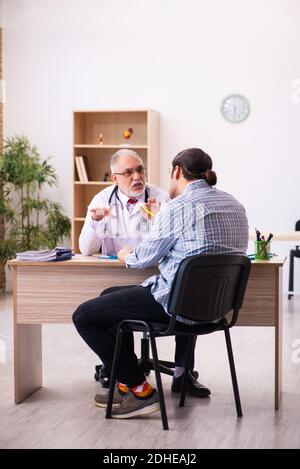 Junger männlicher Patient besucht alten männlichen Arzt Stockfoto