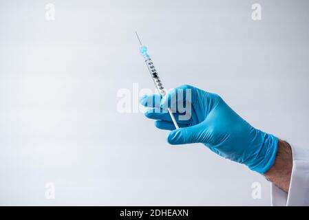 Hand in Handschuh mit einer Spritze mit einem Impfstoff auf weißem Hintergrund. Stockfoto