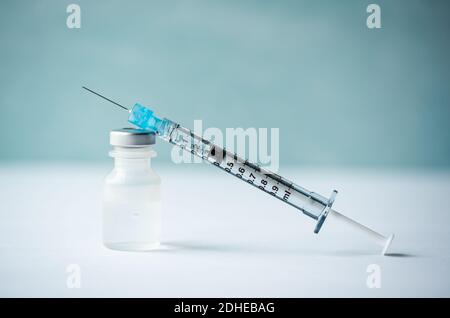 Nahaufnahme von Nadel, Spritze und Fläschchen mit Impfstoff auf weißem Tisch. Stockfoto