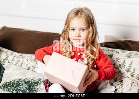 Mädchen mit Geschenk auf Sofa. Kind mit Weihnachtsgeschenk zu Hause. Kind an Weihnachten. Stockfoto