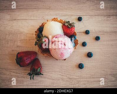 Ein Blick von oben auf zwei Kugeln aus Erdbeere und Vanille Eis in einem Waffelkegel auf einer Holzoberfläche Stockfoto