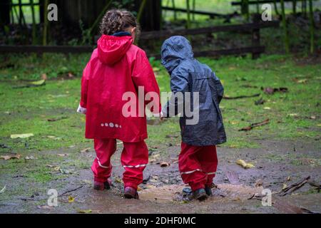 Zwei kleine Kinder, die Spaß haben draußen im Schlamm zu spielen Beim Tragen von kolofuligen Regenmänteln Stockfoto