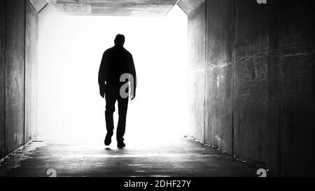 Silhouette des Menschen, die Schultern versenkten beim Gehen aus einem dunklen Tunnel zu einem hellen Licht. Stockfoto