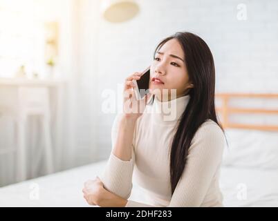 Unglückliche junge Frau, die zu Hause auf dem Handy spricht Stockfoto
