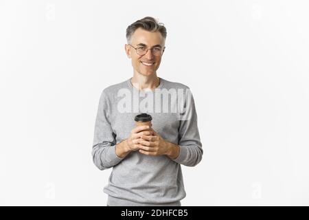 Bild von gutaussehenden Mann mittleren Alters mit grauen kurzen Haaren, tragen Brille und grauen Pullover, Kaffee trinken und lächeln zufrieden, s Stockfoto