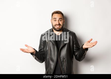 Verwirrt bärtigen Mann in schwarzer Lederjacke fragen um Rat, Blick ahnungslos und zuckend, stehend über weißem Hintergrund Stockfoto