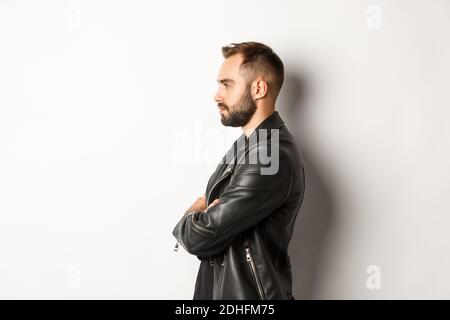 Profil von gut aussehenden seriösen Mann in Lederjacke, Blick nach links, halten die Hände auf der Brust zuversichtlich, weißer Hintergrund Stockfoto