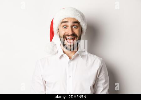 Nahaufnahme von glücklichen bärtigen Kerl in santa Hut, überrascht, feiern weihnachten, stehen über weißem Hintergrund Stockfoto