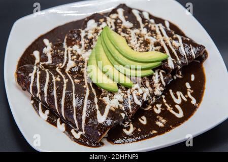 Huhn Enchiladas erstickt in Käse und rote Sauce perfekt auf dem Grill mit Bohnen und Avocado auf der Oberseite vorbereitet. Stockfoto