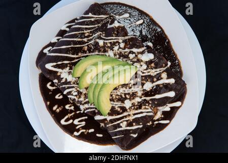 Blick von oben auf Huhn Enchiladas in Käse und rote Sauce perfekt auf dem Grill mit Bohnen und Avocado auf der Spitze zubereitet erstickt. Stockfoto