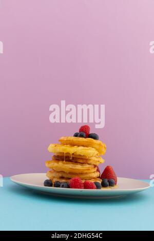 Stapel von Pfannkuchen mit Beeren und Honig auf blau und Rosa Hintergrund Stockfoto