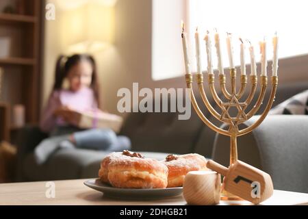 Menorah, Dreidel und Donuts auf dem Tisch des glücklichen kleinen Mädchens, das Hannukah zu Hause feiert Stockfoto