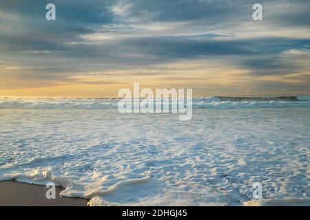 Sonnenuntergang über dem Meer. Stürmische Wellen und Meeresschaum am Strand mit schönen bewölkten Himmel im Hintergrund Stockfoto