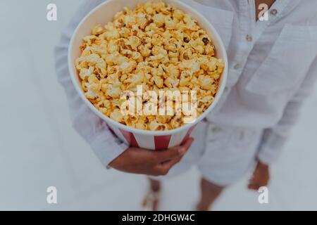 Nahaufnahme eines jungen süßen Mädchens, das eine Tube Popcorn in den Händen hält. Stockfoto