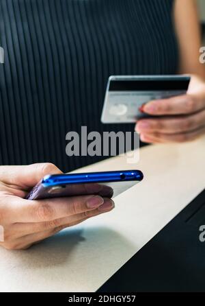 Eine Nahaufnahme der Hände einer Frau, die eine Kreditkarte hält und Online-Transaktionen mit Handy-Konzept E-Commerce, Mobile Banking Stockfoto