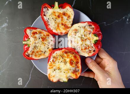 Hand Holding a Plate of Delicious Homemade Stuffed Bell Peppers Placing on Black Marble Table Stockfoto