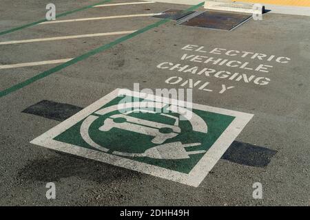 Laden von Elektrofahrzeugen nur in schablonierten weißen Buchstaben auf dem Bürgersteig eines EV-Ladeplatzes auf einem Parkplatz; Symbol für EV-Ladegrafik. Stockfoto