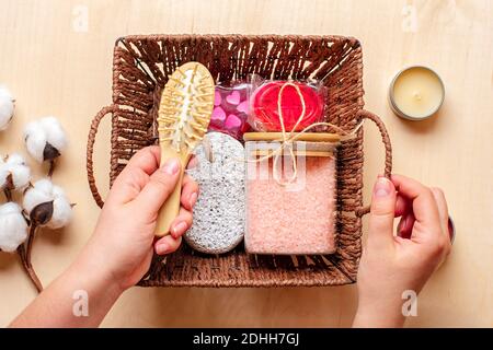 Weibliche Hand hält Pflegebox Set aus umweltfreundlicher Kosmetik Badesalz, Holzkamm, Bimsstein, Duftkerzen, handgemachte Seife, Waschschwamm auf Stockfoto