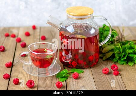 Kräutertee mit Beeren, Himbeeren, Minzblättern und Hibiskusblüten in Glas Teekanne und Tasse auf Holztisch Medizin für kaltes Vitamin Drink Rustikal Stockfoto