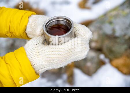 Weibliche Hände in Handschuhen halten heißen Tee, Stockfoto