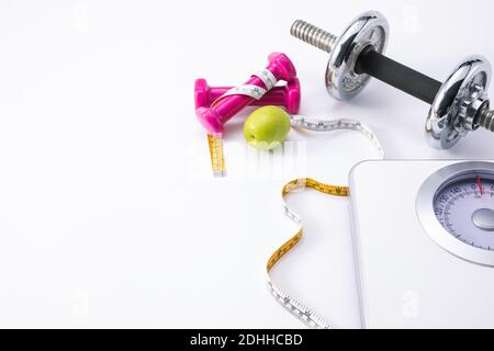 Eine Fitness-Komposition mit rosa Hanteln, grünem Apfel, Maßband und Waage Stockfoto