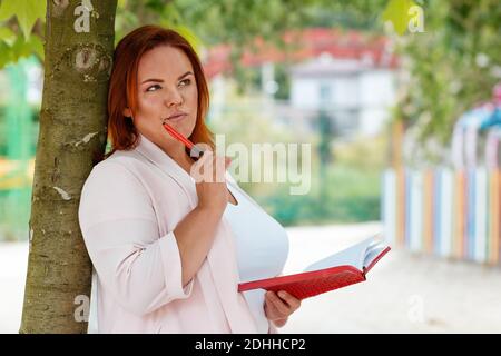 Freiberuflich. Porträt einer kaukasischen nachdenklichen Frau mit einem Notizbuch und Stift, kommen mit einer neuen Idee. Plus-Modell. Im Freien. Konzept der Fernbedienung Stockfoto