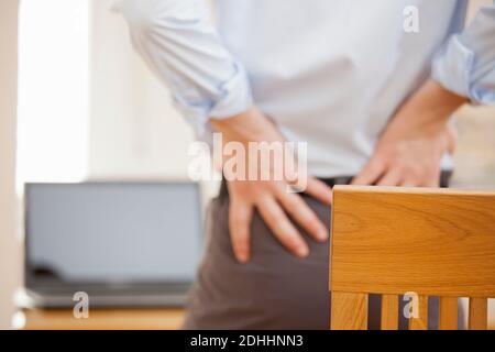 Geschäftsmann mit Rückenschmerzen stehen vor seinem Arbeitsplatz während Arbeiten von zu Hause aus – selektiver Fokus Stockfoto