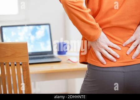 Mann mit Rückenschmerzen, der von zu Hause aus mit einem Laptop arbeitet - Konzentrieren Sie sich auf die Hände Stockfoto